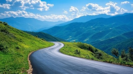 Fototapeta premium A winding asphalt road through green mountain scenery, with a clear blue sky and light, scattered clouds on a sunny day.