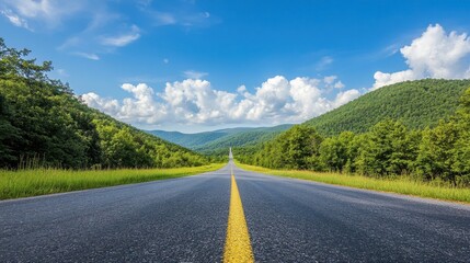 Fototapeta premium An asphalt road stretching towards green mountains, with a bright blue sky and puffy clouds on a sunny, clear day.