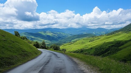 Naklejka premium An asphalt road winding through green mountain valleys, with a clear sky and soft white clouds on a sunny, bright day.