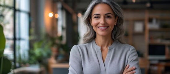Portrait of a confident, middle-aged woman smiling with her arms crossed, standing in a modern office setting.
