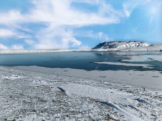 Lake in the winter with snow on the ground and a mesa in the background 