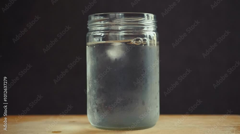 Poster ice cubes splashing into a glass jar filled with water, creating ripples and movement