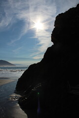 Looking out over the Pacific ocean seas at the sun with waves breaking and a black rockface in front