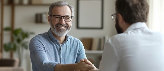 Obraz premium Smiling man in a blue shirt shaking hands with a colleague during a meeting in a modern office.
