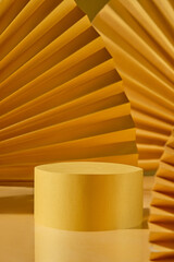 On a reflecting table, a cylinder block with room for product display is positioned next to designs made of yellow paper fans. A luxurious area with a backdrop of copper.