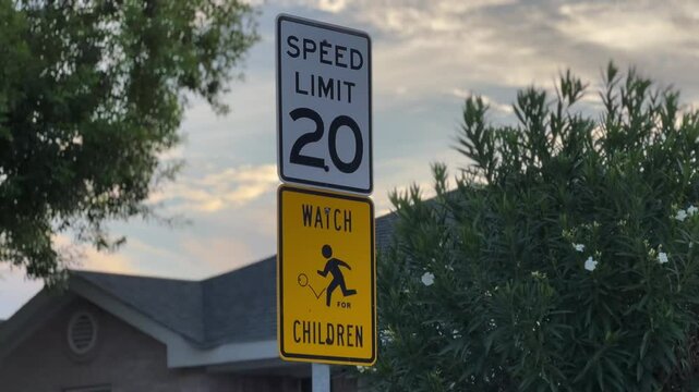 A traffic sign for a speed limit of 20 mph with another sign of watch children in yellow located in a corner of a street in a neighborhood