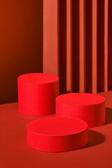 Three red cylindrical platforms, arranged in a minimalist manner against a backdrop of red vertical stripes, create a harmonious image. The platforms offer space to showcase various products.