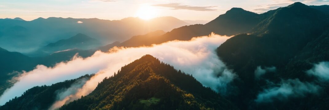 Aerial view of a mountain range with the sun setting behind it, casting a warm glow over the clouds that blanket the landscape. This serene scene evokes feelings of tranquility, adventure, and the bea