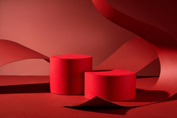 The image is ideal for presenting products, featuring two red cylindrical podiums on a red background, curled and arched over by a large piece of red paper curled and arched over them.