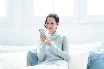 リビングのソファで携帯を持つ笑顔の女性