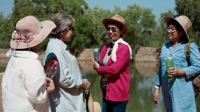 Best friends, group elderly Asian women have been close for long time, let's travel nature during day when sun is bright but weather is good, standing talking, resting, tired, holding water in hand.