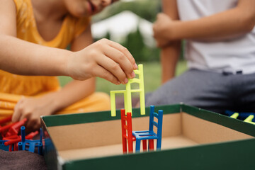 Close-up of children playing a colorful stacking board game outdoors. Engaging and fun activity emphasizing teamwork and creativity.