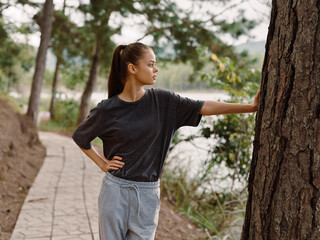 Thoughtful young woman standing by a tree while enjoying nature, wearing comfortable gray clothing, reflecting on life with a serene expression