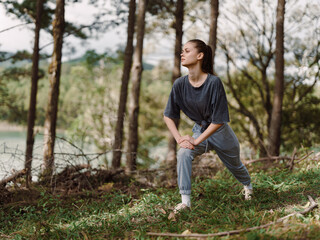 Young woman in gray sportswear stretching in a tranquil forest, practicing mindfulness and fitness in nature Wellness and active lifestyle concept