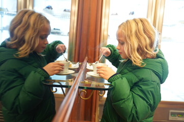 Little blonde in a green jacket drinks cappuccino in bar in Italy