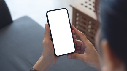 Cell phone white blank screen mockup, woman's hand holding mobile phone with blank screen and a cup of coffee in coffee shop, over shoulder view