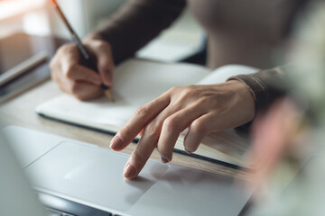Close up, business woman writing note on notebook and using laptop computer to search the...