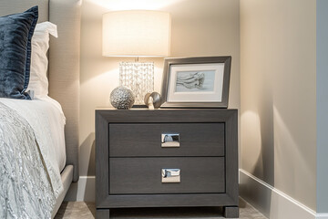 A gray wooden bedside table with two drawers and an open photo frame on top, placed next to the bed in a bedroom designed for senior living, showcasing modern design elements and clean lines.