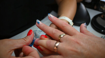 A beautician applies blue glitter to a woman's nail polish in a nail salon