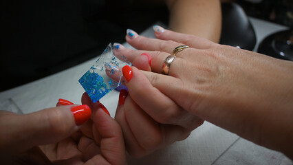 A beautician applies blue glitter to a woman's nail polish in a nail salon