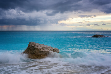Waves crashing on a rock in the sea with turquoise water with a storm