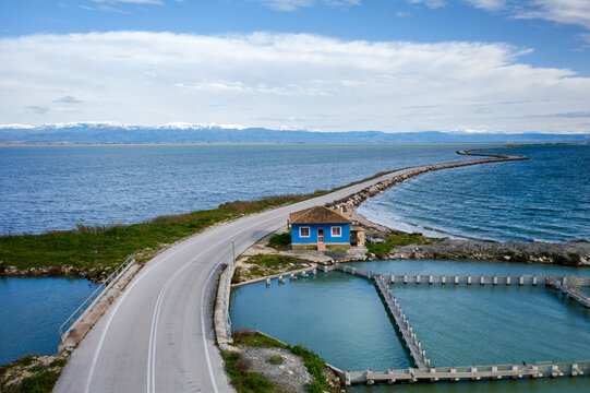 Drone view of blue house on road with curves between two lakes, Greece