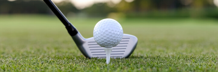 A golf ball is on a tee and a golf club is next to it. The ball is white and the club is silver