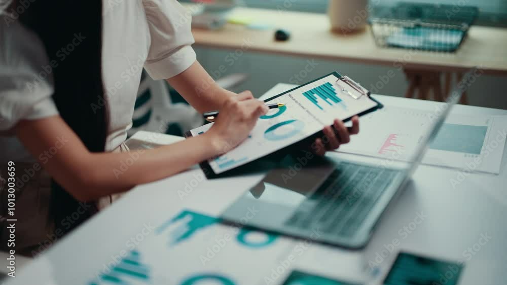 Poster businesswoman is sitting at her desk and analyzing financial charts on a clipboard. she is using a p