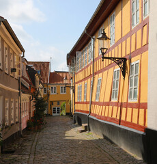 north danish house with small square paned windows and a scraped stucco facade on a narrow cobblestone street without people