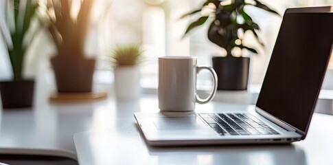 Minimalist white office desk with laptop and coffee mug on a blurred background, with space for text, representing the concept of working from home