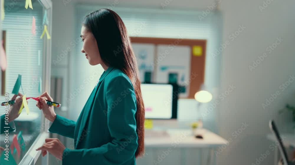 Poster Young businesswoman is analyzing data and connecting points drawn on a transparent board with colorful markers in an office