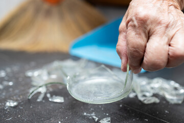 Old elderly holding a piece of broken glass, pick up broken glass with bare hand during sweeping or...