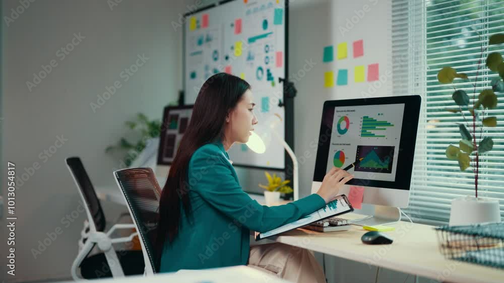 Aufkleber young asian businesswoman analyzing financial data on computer and taking notes on notebook. she's w