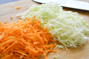 Grated carrots and cabbage on chopping board. Coleslaw salad preparation. 