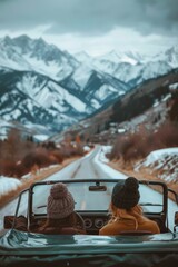 Two friends drive along a winding mountain road surrounded by snow-capped peaks during a cloudy winter day. View from the back. Place for text