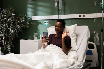 In the hospital room, a young African patient relaxes with her phone, watching a movie or a TV show.