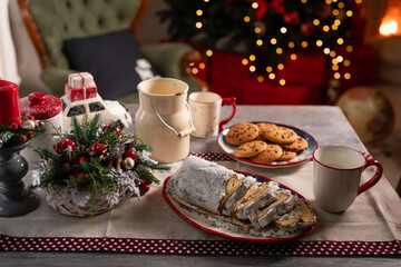 Christmas table with stollen cake, cups, cookies on the background of decorated Christmas tree and fireplace, Cozy Christmas atmosphere