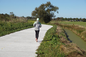 Jogger on Dutch cycle path with new road surface, ditch, meadows. Blue sky. Autumn, October,...