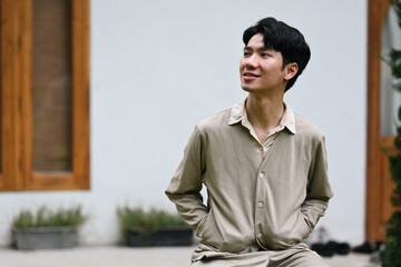 Portrait of a confident man gazing upward with a soft smile, dressed in light-toned casual wear, against a minimalist cabin background