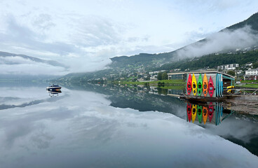 Colourful kayaks mirror reflection on peaceful mountain lake in misty morning, patches of snow.