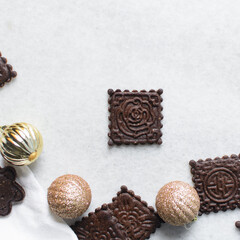 Overhead view of stamped molasses cookies and gold Christmas ornaments on a parchment lined baking tray, top view of embossed gingerbread cookies and gold Christmas baubles on a white background