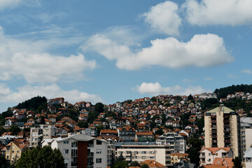 View of the old mountain houses with red tiled roofs and high-rise buildings in the Yugoslavian style. Small town Uzice in the south of Serbia. A sunny day, clouds in a blue sky.