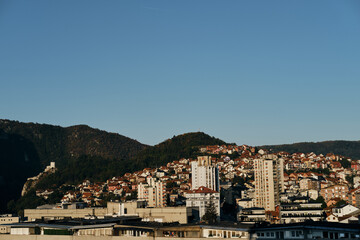 View of the old mountain houses with red tiled roofs and high-rise buildings in the Yugoslavian style. Small town Uzice in the south of Serbia. Clear blue morning sun.