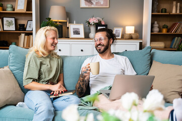 Obraz premium Leisure people concept happy couple enjoying free time at home for bonding. Man and woman boyfriend and girlfriend or roommate free time on sofa reading and surfing the internet. Weekend activities