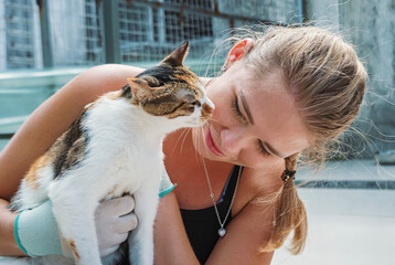 A young woman bonding with a friendly cat at an animal shelter during a sunny afternoon visit to...