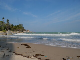 The beach is a breathtaking sight, with soft, powdery white sand stretching as far as the eye can see. The water is a mesmerizing shade of clear blue, sparkling under the bright sun, inviting you to