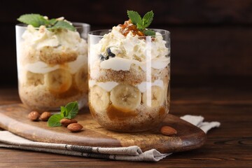 Tasty trifle dessert. Sponge cake, banana and whipped cream in glasses on wooden table, closeup