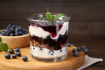 Tasty trifle dessert. Blueberries, sponge cake and whipped cream in glass on wooden table