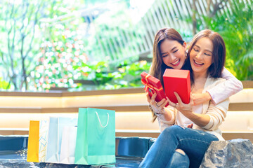 Happy Asian daughter give gift box to mature mother during shopping together at shopping mall. Mom...