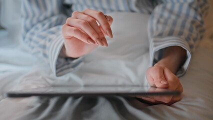 Fototapeta premium Woman hands swiping tablet on cozy white bed closeup. Woman planning work on pad